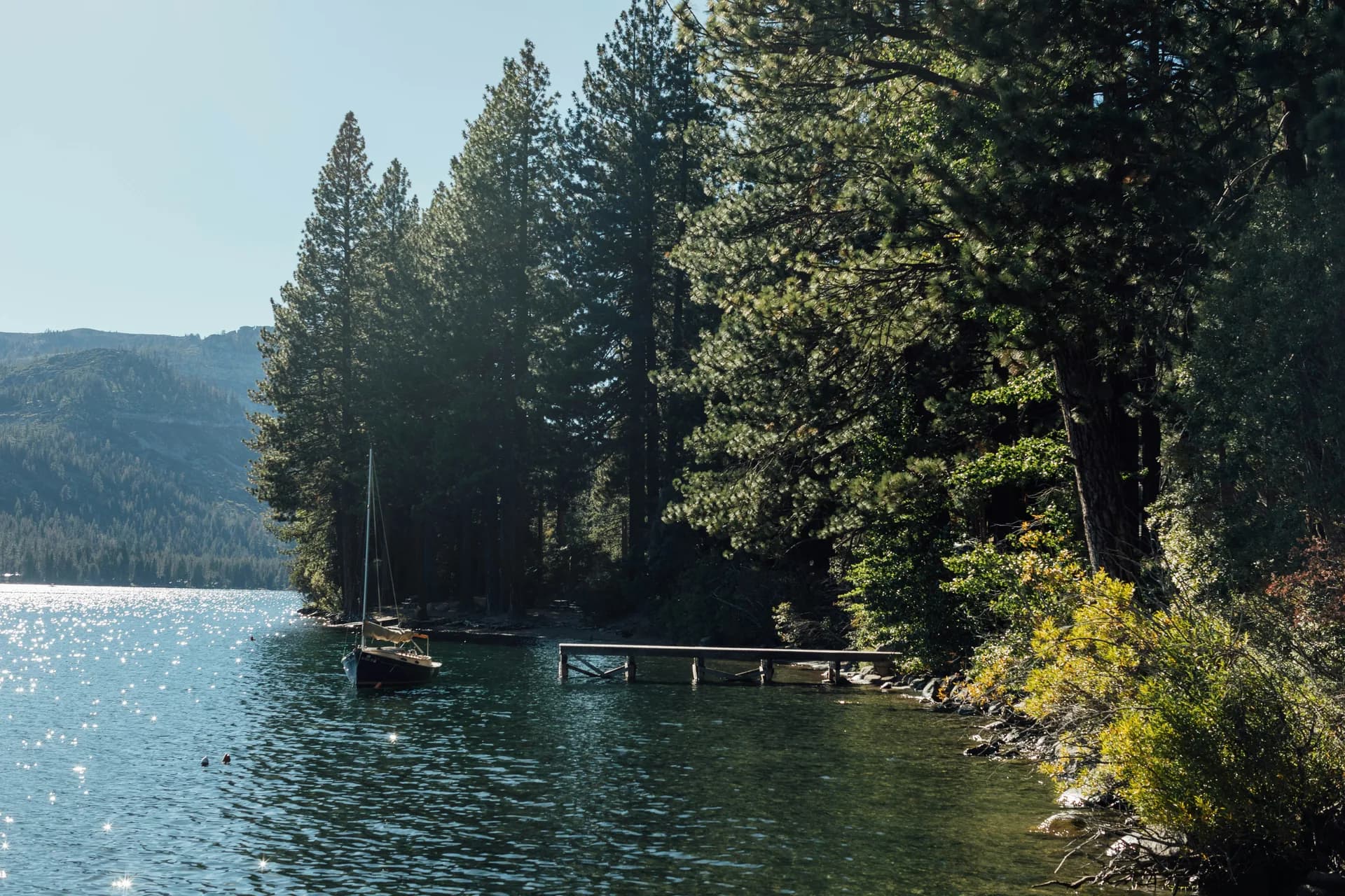 A wooden dock and a moored sailboat in a quiet cove on Lake Tahoe, pines along the shore