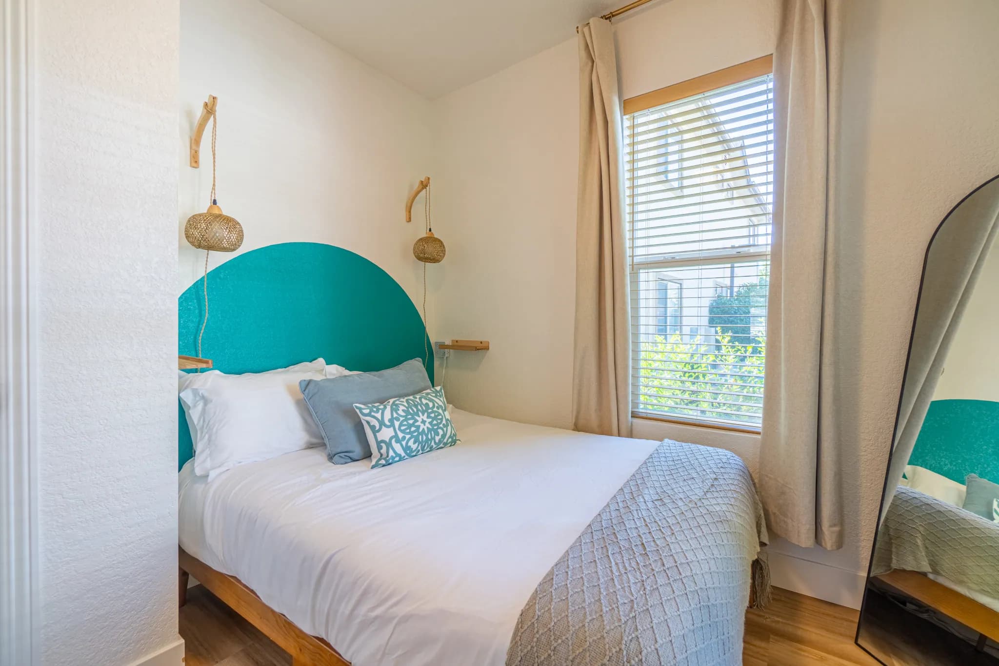The same small Litch Court bedroom with a queen bed against a painted teal arch and hanging rattan pendant lights